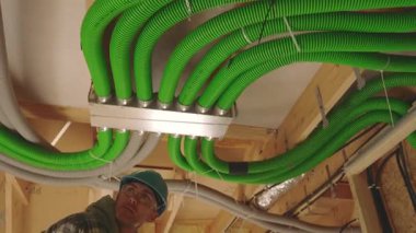 Bir inşaat alanında, bir işçi dikkatlice havalandırma havalandırma sistemi kurar. Kabloları hizalamaya odaklanıyor, binadaki etkili elektrik işleri için düzgün bir şekilde güvence altına alınmasını sağlıyor..