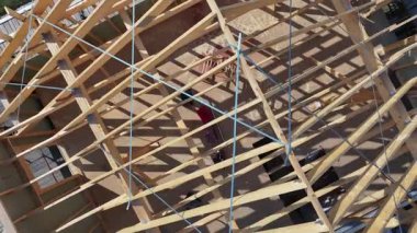 İşçiler inşaat alanında ahşap bir yapı inşa etmekle meşguller. Karmaşık çerçeve dikkatli planlama ve işçiliği ortaya koyuyor. Proje güneşli bir açık hava ortamında etkin bir şekilde ilerlerken araçlar kullanılıyor.