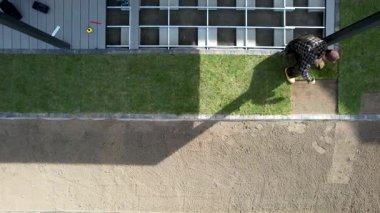 Bir işçi, yerleşim alanına çağdaş bir peyzaj tasarımı yerleştirirken görülüyor. Bölge düzgünce düzenlenmiş çimen ve patikalara sahip..
