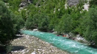 Deneyimli kayakçılar yemyeşil ve kayalık oluşumlarla çevrili canlı bir turkuaz Soca nehrinde yol alırlar. Slovenya, Avrupa.