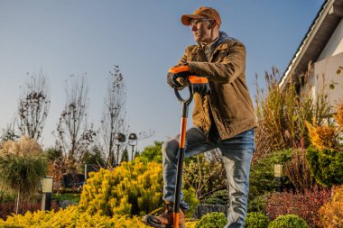 Bir bahçıvan elinde bir kürekle özgüvenle duruyor, yemyeşil, renkli bir bahçeyi inceliyor. Günbatımının sıcacık parıltısı etrafındaki canlı bitkileri vurguluyor. Bir sonraki adımlarını planlarken sakin ve üretken bir atmosfer yaratıyor..