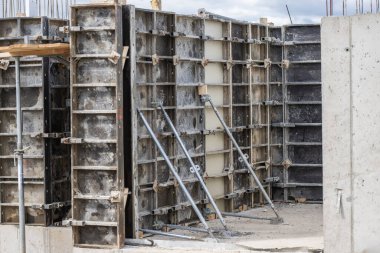 Beton yapılar, beton dökme kalıplarının montajını gösteren bir inşaat sahasına kuruluyor. Çelik takviye ve iskele işçiler inşaatın bir sonraki aşamasına hazırlanırken destek sağlıyor.