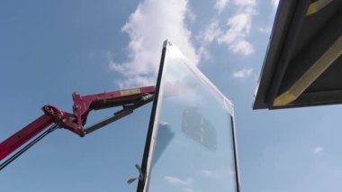 İnşaat işçileri Parlak Güneş Işığındaki İnşaat Alanında Crane kullanarak Büyük Cam Paneli Kaldırıyor