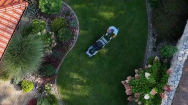 Bahçıvan, güneşli öğleden sonra bahçedeki yemyeşil çimenleri biçiyor.