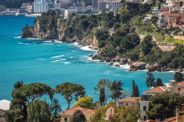 15 Mart 2025 Monte Carlo, Monaco. Kıyı şeridinde büyüleyici turkuaz sular var. Yeşilliklerle bezenmiş kayalık kayalıklara hafifçe çarpıyor..