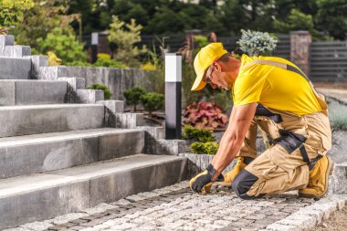 Yetenekli işçiler, parlayan güneş ışığı altında yeşil alanların bulunduğu patikaya taş kaldırımları dikkatlice yerleştiriyor..