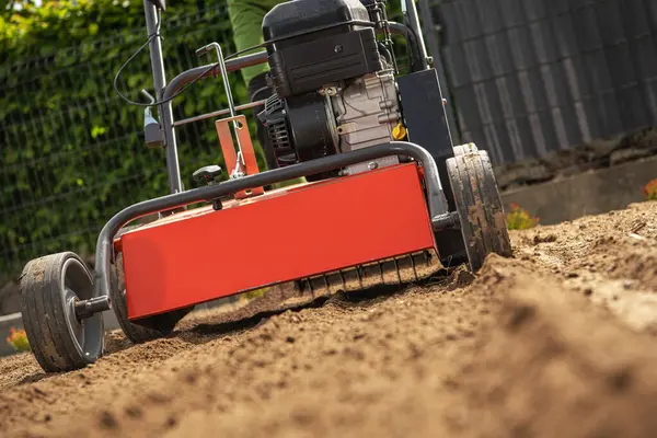 Bir bahçıvan sebze bahçesinde toprak dümeni işletiyor, uygun bir ekme yatağı yaratmak için toprağı çeviriyor. Taze toprak bahar ekimi için havalandırılıyor..