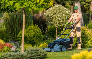 Bir bahçıvan, parlak gün ışığında renkli çiçekler ve yeşilliklerle çevrili güzel bir bahçedeki çimleri biçer..