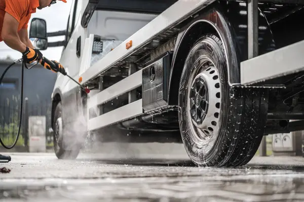 Bir işçi, bir benzin istasyonunda ticari bir kamyonun tekerlerini temizlemek için basınç makinası kullanır. Böylece aracın en iyi şekilde çalışmasını sağlar..