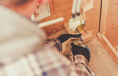 Yetenekli bir elektrikçi, konut inşaatındaki bir bağlantı kutusuna kablo döşemeye odaklanır. Güvenli kurulumu sağlamak için eldiven ve aletler kullanıyor..