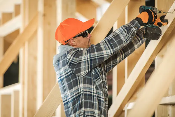 Bir inşaat işçisi, inşaat alanında ahşap kirişlere koruyucu dişli matkaplar takıyor, marifetli bir işçilik sergiliyor ve güvenliğe odaklanıyor..