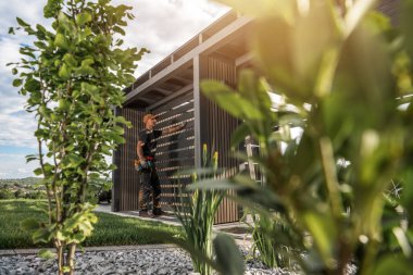 Bir işçi, çağdaş bir bahçe yapısına tahta levhalar yerleştirmeye odaklanır. Yeşilliğin etrafını sarmak kırsal kesimin sakin atmosferini arttırır..