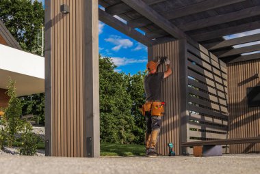 Bir inşaat işçisi dışarıdaki bir çerçeveye ahşap panellere aydınlatma armatürü yerleştiriyor. Güneşli bir günde konut alanında marifetli bir işçilik sergiliyor..