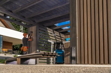 Yetenekli bir işçi, çeşitli aletler kullanırken çağdaş bir açık hava yapısına ışık armatürü yerleştiriyor. Parlak gün ışığı etkinliği arttırır ve ayarlar..