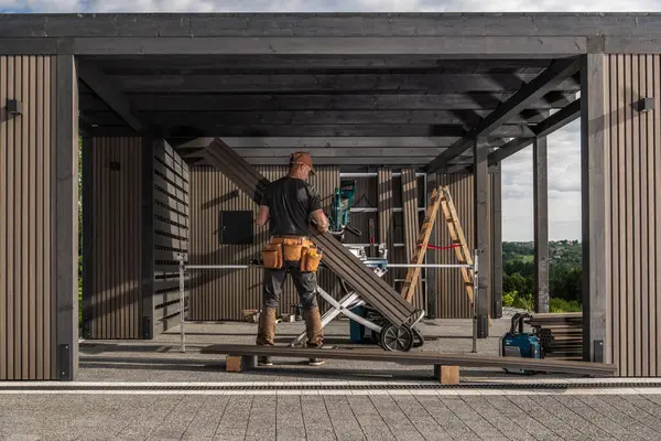 Bir inşaat işçisi dışarıda ahşap bir garaj inşaatı yapmakla meşgul. İşine odaklanırken etrafını aletler ve malzemeler sarmış..