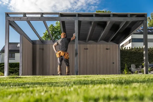 Bir inşaat işçisi çimenli bir bahçede duruyor, açık bir günde yeni inşa edilmiş bir dış yapıyı çağdaş bir tasarımla değerlendiriyor..