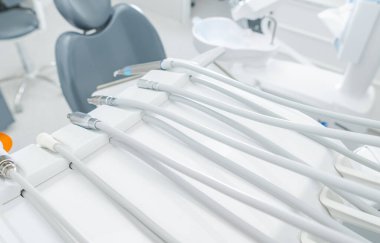 Parlak bir klinikteki bir çalışma istasyonunda sıradaki hastayı bekleyen çeşitli diş aletleri. Çevre temiz ve düzenli..