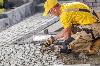 Yetenekli bir işçi, açık havada, parlak bir gökyüzünün altında çalışırken dikkatle kaldırıma kaldırım taşları serer..