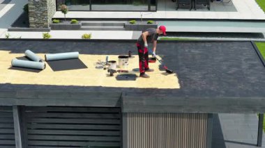 Kalifiye bir işçi, açık havada çağdaş bir binaya EPDM çatı malzemesi yerleştirirken görülüyor. Çatı alanı görev için araçlar ve malzemelerle donatılmıştır.