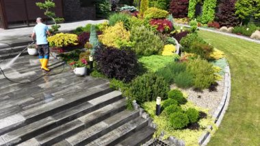 40 'lı yaşlarındaki beyaz adam avluda temizlik yapıyor. Basınç Makinesi kullanıyor.