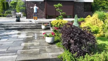 Bahçıvan teras yüzeyini basınçlı çamaşır makinesiyle temizlerken aynı zamanda peyzajı canlı bitkiler ve düşünceli tasarım elementleriyle güçlendiriyor..