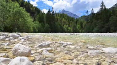 Sakin bir nehir bulutlarla benekli mavi bir gökyüzünün altındaki yoğun yeşil ağaçların arasından süzülür. Seksi, İtalya.