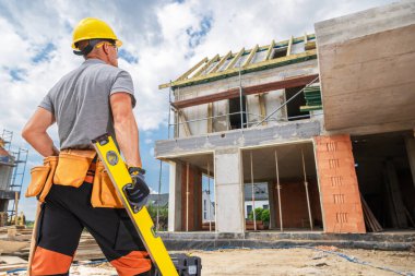 Bir inşaat işçisi, elinde bir aletle neredeyse bitmiş bir binayı gözetliyor. Proje aktif, yapım aşamasını gösteriyor.