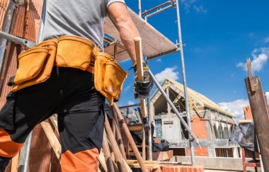 Bir inşaat işçisi işe hazırlanırken, gün içinde yoğun bir şantiyede inşaata nezaret ederken aletlerle de ilgilenir. Parlak gökyüzü verimliliği artırır.