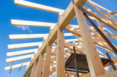 İşçiler bir inşaat sahasına sağlam ahşap kirişler dikiyorlar, parlak mavi bir gökyüzünün altında iskeleti sergiliyorlar. Yapı şekilleniyor..