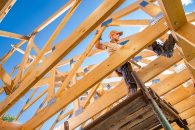 Bir inşaat işçisi, açık mavi gökyüzünün altındaki bir inşaat projesinde çalışırken ahşap kirişleri ustalıkla yönetir..