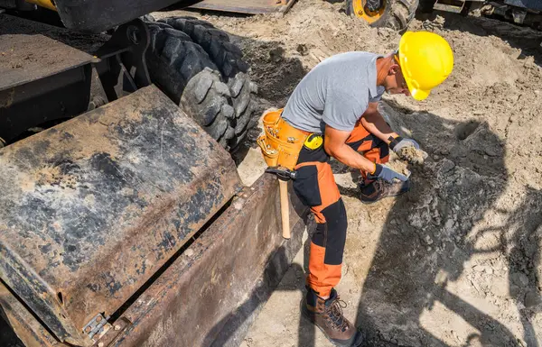 Sarı başlıklı bir inşaat işçisi, yoğun bir inşaat sahasının zeminini incelemek için bir araç kullanarak kazı yapıyor..