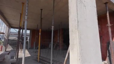 İşçiler, duvarları kısmen dikilmiş ve parlak bir gökyüzünün altında yapı iskelesi olan yeni bir binanın şekillendiği bir inşaat alanında meşguller..