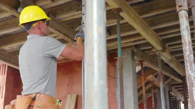 Sarı kasklı bir işçi inşaat alanında ahşap kirişleri koruyor. Bu çalışma, yapısal bütünlük ve güvenliğin sağlanması için gereklidir..