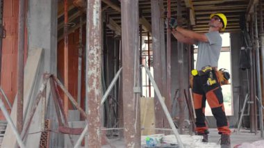 Güvenlik teçhizatı giymiş bir işçi, yapısal unsurlar ve araçlarla ilgili görevlere odaklanarak, gün boyunca bir şantiyede inşaat faaliyetlerine katılır..