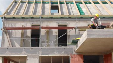 İşçiler açık gökyüzünün altında yeni bir konut inşaatı ile meşgul. Malzemeleri yerleştiriyorlar ve tamamlanmak için duvarları hazırlıyorlar..