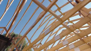 İnşaat işçileri yeni çatıyı ahşap kirişlerle donatıyorlar. Detaylı işçilik ve güneşli hava sergiliyorlar. Ağaçlar arka planda görünür..