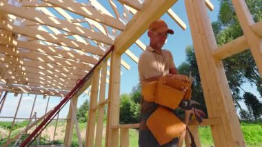 Becerikli marangoz, yemyeşil ve inşaat aletleriyle çevrili güneşli gökyüzünün altında ahşap bir iskelet birleştirir..