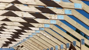 Ahşap kirişler açık mavi gökyüzünün altında inşa ediliyor, istikrar için kullanılan çerçeve ve metal konnektörlerin detaylarını gösteriyor.