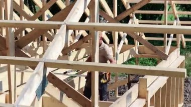 Yetenekli bir zanaatkar, açık bir günde inşaat alanındaki ahşap kirişleri ölçüyor ve ayarlıyor. İnşaat sürecini doğal bir ortamda gösteriyor..