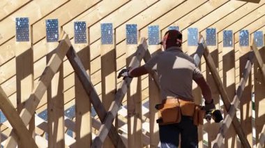 Bir inşaat işçisi, ahşap hortum iskeletini dikkatlice birleştirir, yoğun güneş ışığı altında maharetli işçilik sergilerken, aynı zamanda bölgede hassasiyet ve güvenliği sağlar..