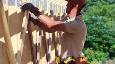 Bir inşaat alanında ahşap iskelet inşa eden bir adam, yeşil bir arazide açık mavi bir gökyüzü altında yeteneğini ve dikkatini gösteriyor..