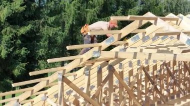 Becerikli bir işçi, güneşli bir günde verimli yeşil bir arazide ahşap bir çatı iskeleti inşa eder, hassas aletler kullanır..