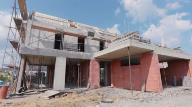 İşçiler modern bir ev inşa ediyorlar. Çerçeveleme ve duvarcılık çalışmalarını açık mavi gökyüzü altında sergiliyorlar..