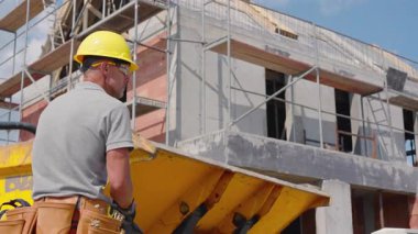 Miğferli ve gömlekli inşaat işçisi inşaat alanında makine çalıştırıyor. Proje, hareketli bir kentsel alanda konut geliştirmeyi içeriyor..