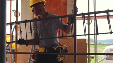 Bir inşaat işçisi, arka planda güneş parlarken güvenli bir operasyona odaklanmış metal takviyeleriyle uğraşıyor..