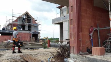 Bir inşaat işçisi, arka planda bulutlu bir gökyüzünün altında yapı iskelesi ve malzemelerle birlikte bir inşaat alanının ilerlemesini gözlemler..