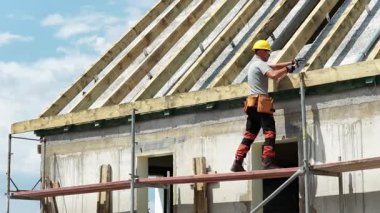 Yetenekli işçiler bir inşaat sahasında çatı montajını denetliyor, güvenlik önlemleri ve takım çalışması sergiliyor. Parlak gökyüzü aktif çalışma ortamını güçlendirir.