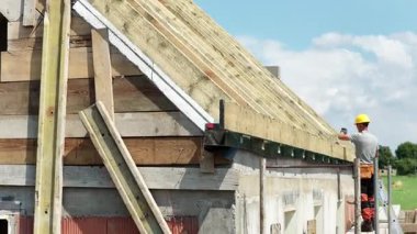 İşçiler aktif bir inşaat sahasında yeni bir binanın çatısını inşa ederken, yukarıda güneş parlayarak projede kaydedilen ilerlemeyi vurguluyorlar..