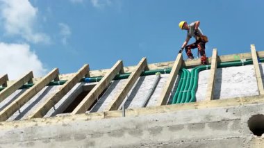 Bir inşaat işçisi mavi gökyüzünün altındaki bir çatıya yeşil borular yerleştiriyor ve düzgün bir drenaj sağlama üzerine yoğunlaşıyor..
