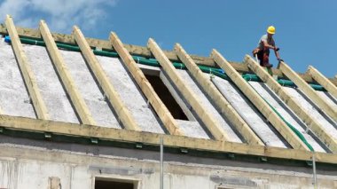 İşçiler, güneşli bir günde projenin bir sonraki aşamasına hazırlanırken yeni inşa edilmiş bir binanın üzerine çatı malzemeleri seriyorlar..